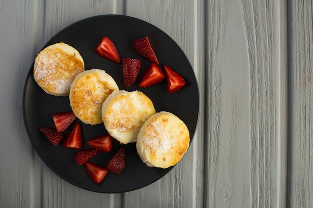 Cheese pancakes and  strawberries on the dark plate on the grey wooden background.Top view.Copy space.