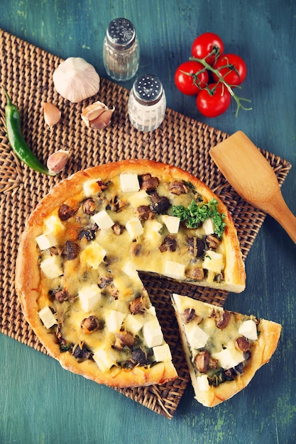 Cheese pie with mushrooms herbs and sour creme on wicker mat on wooden table background