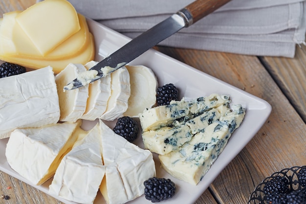 Cheese plate. Assortment of cheese with berries on wooden background.