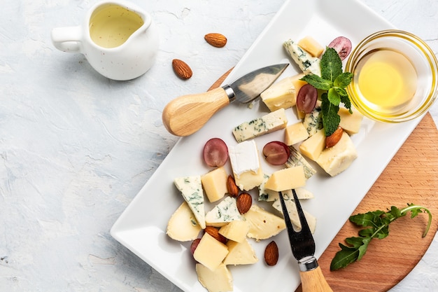 Cheese plate assortment of various types of cheese with grapes, honey and nuts, top view.