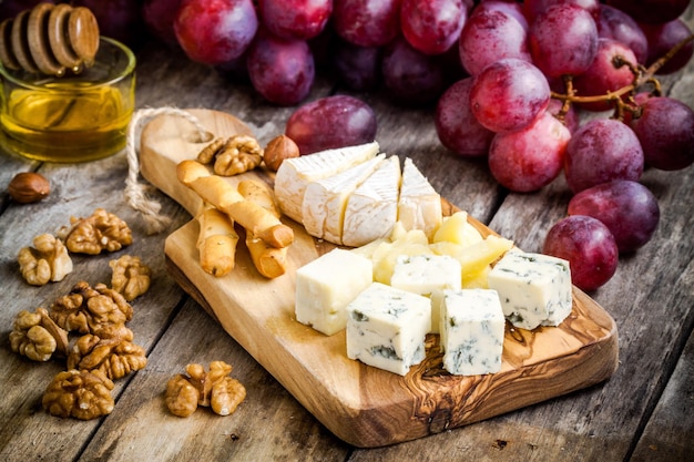 Cheese plate Camembert Parmesan blue cheese bread sticks walnuts hazelnuts honey grapes on wooden table