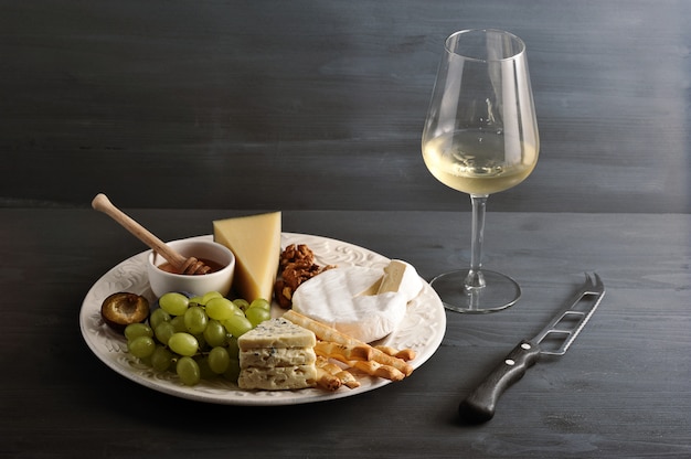 Photo cheese plate, wine and cheese knife on dark  