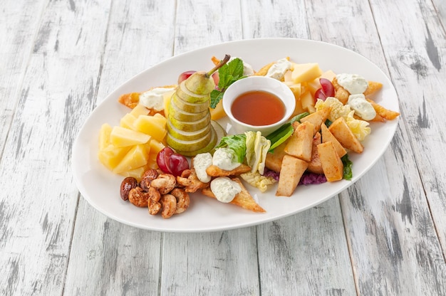 Cheese plate with pear, wheat chips and pesto sauce. In a white plate. Light wooden background. View from above