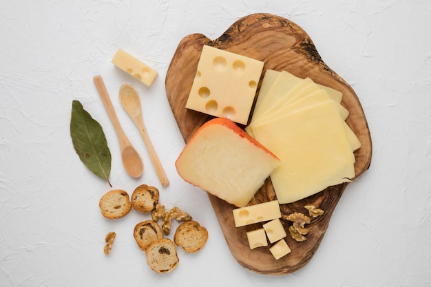 Cheese platter with bread slice; bay leaf and walnut over white surface