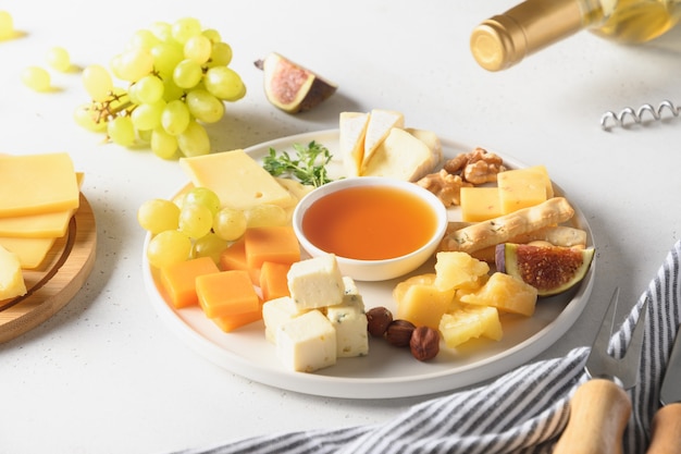 Cheese platter with grapes nuts figs on white background