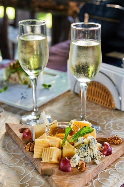 Cheese platter with honey walnuts and grapes and two glasses of champagne on a table in a cafe