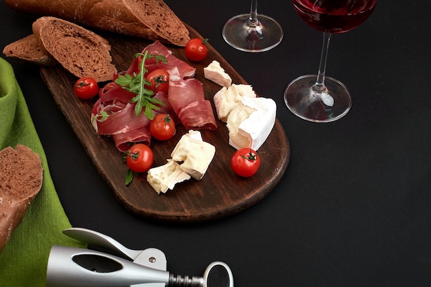 Cheese prosciutto bread vegetables and spices on wooden board on black background with copy space