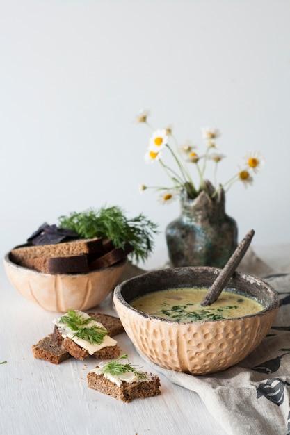 Cheese soup with mushrooms and vegetables, brown bread with butter, dill and basil on white wood