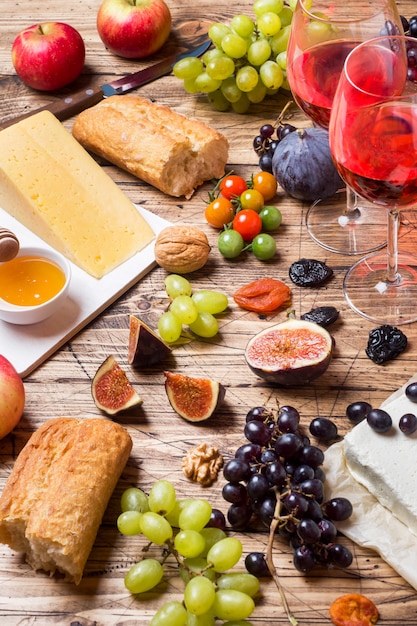 Cheese, wine, baguette grapes figs honey and snacks on the rustic wooden table top.