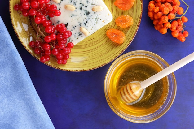 Cheese with honey and a blue napkin on a blue background Blue cheese with nuts berries and dried fruits on a yellow plate Closeup View from above