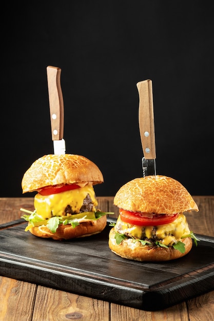 Cheeseburgers with tomatoes and arugula on a black wooden board close up