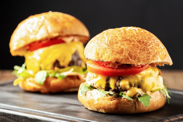 Cheeseburgers with tomatoes and arugula on a black wooden board close up