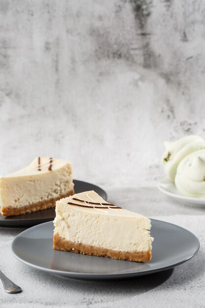 Photo cheesecake new york or classic cheesecake with cup of coffee on white table. closeup view. tasty breakfast. piece of cake on black plate, white cup on white marble background. vertical photo.