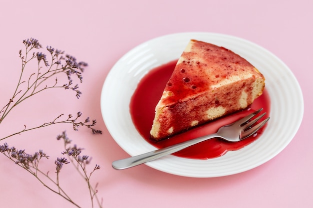 Cheesecake on a white plate with strawberry sauce, on a light pink background.