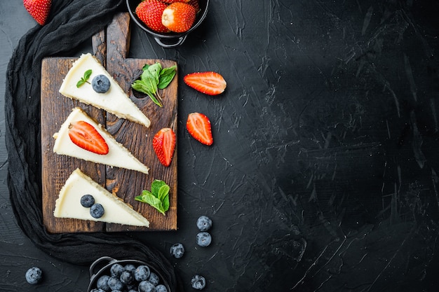 Cheesecake with blueberries and strawberries, on black table, top view flat lay