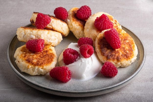 Cheesecakes or syrniki on a round plate with raspberry, sour cream and raspberry syrup.