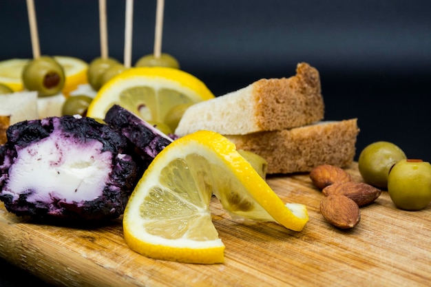 Cheeses lemon and olives with bread on older wooden cutting board A serving antipasto on older wooden chopping board