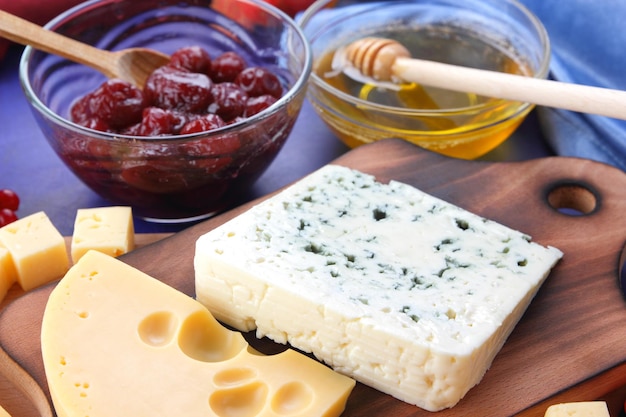 Cheeses with honey and lemon on a blue background with blue and red napkins Two types of cheese on a wooden board with fruits and berries closeup