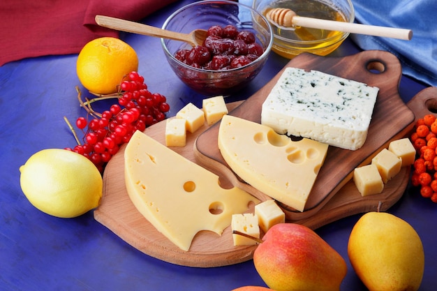 Cheeses with honey and lemon on a blue background with blue and red napkins Two types of cheese on a wooden board with fruits and berries closeup