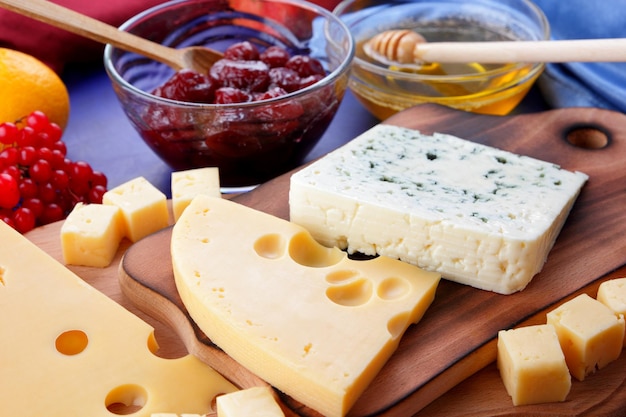 Cheeses with honey and lemon on a blue background with blue and red napkins Two types of cheese on a wooden board with fruits and berries closeup