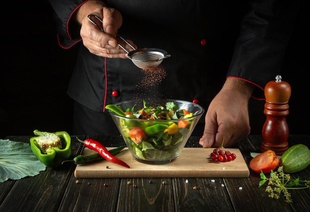 The chef adds flavoring to the vegetable salad Vegetarian food by hands of the cook in the kitchen Menu idea for a hotel or restaurant