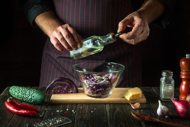 The chef adds olive oil to fresh red cabbage salad in a restaurant kitchen