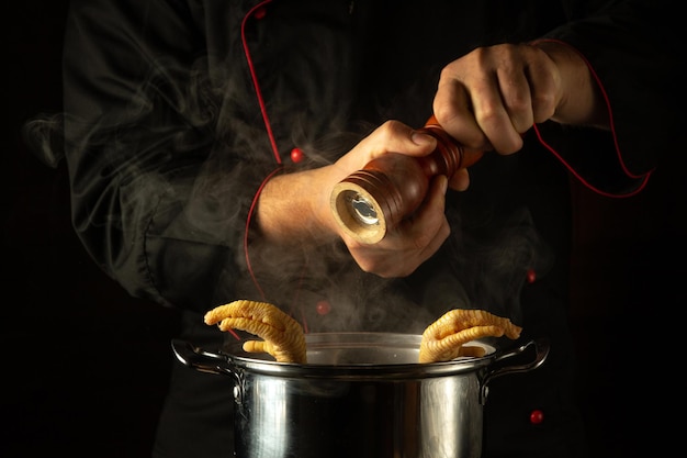 The chef adds pepper to a pot of boiling chicken legs