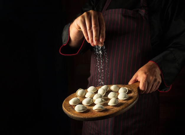 The chef adds salt to meat dumplings on a cutting board Concept for a hotel menu