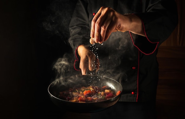 The chef adds salt to a steaming hot pan