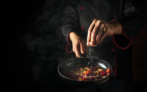 The chef adds salt to a steaming hot pan