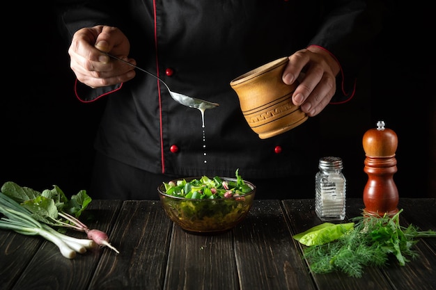 The chef adds sour cream to a fresh vegetable salad Cooking delicious food in the kitchen