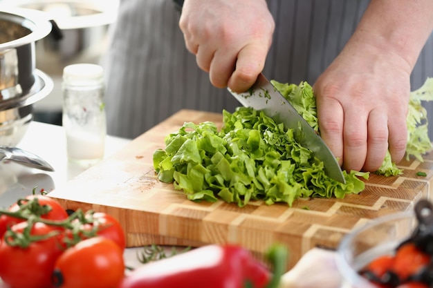 Chef in an apron cuts vegetables and green salad