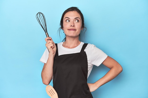 Chef in apron holding manual whisk ready to mix on blue