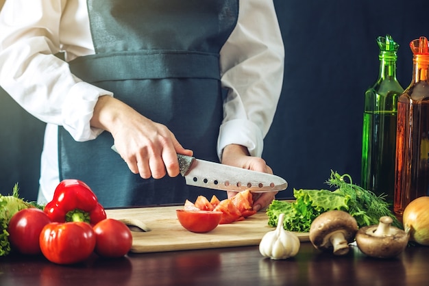 Chef in black apron cutting vegetables