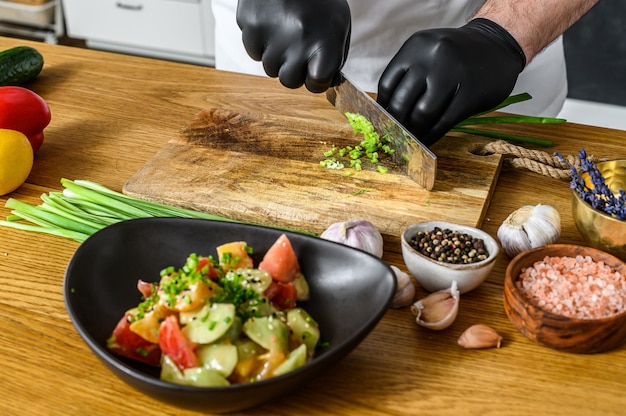 A chef in black gloves is slicing fresh green onions on a wooden chopping Board. Concept of cooking healthy organic food