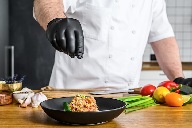 The chef in black gloves prepares tartare from fresh tuna