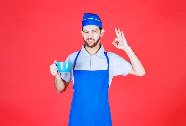 Chef in blue apron holding a blue ceramic cup and enjoying the taste of the product. 