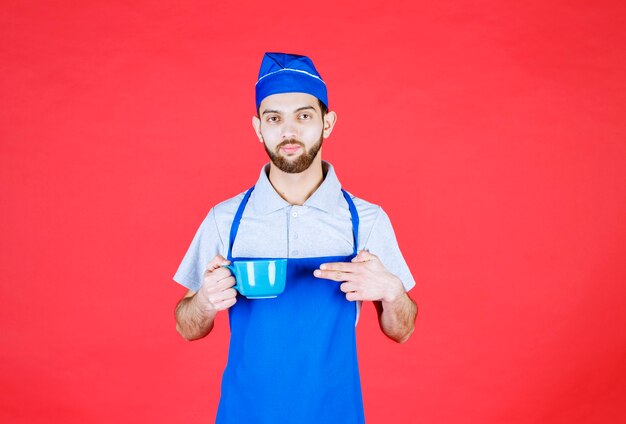 Chef in blue apron holding a blue ceramic cup. 