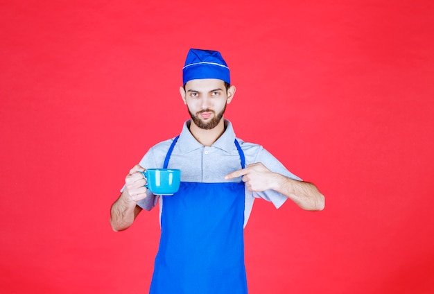 Chef in blue apron holding a blue ceramic cup. 