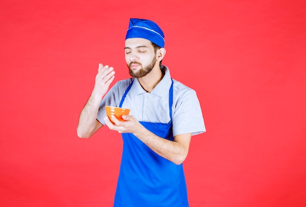 Chef in blue apron holding a yellow ceramic cup and smelling the food. 