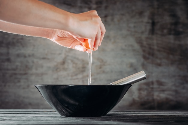 Chef breaks eggs into black bowl on wooden table