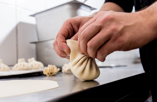 Chef coocking georgian khinkali or japanese wonton. Traditional meal of dough and meat. National cuisine, cooking process. Restaurant kitchen.