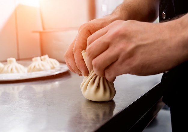 Chef coocking georgian khinkali or japanese wonton. Traditional meal of dough and meat. National cuisine, cooking process. Restaurant kitchen.