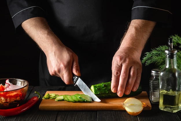 Chef or cook cutting a green cucumber in kitchen in the restaurant. Making a delicious salad with fresh vegetables