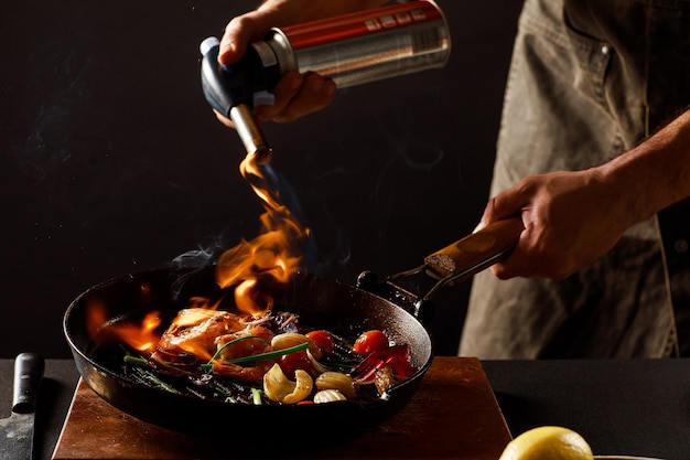 Chef cooks with fire in a pan shrimp with vegetables