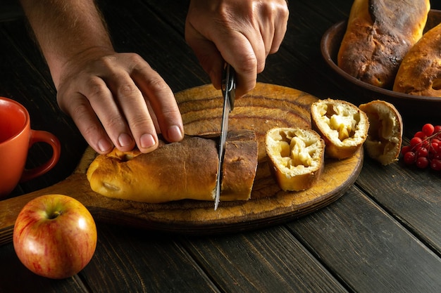 The chef cuts an apple pie freshly baked in a bakery on a kitchen cutting board before drinking tea The national dish is served at the festive table for dinner