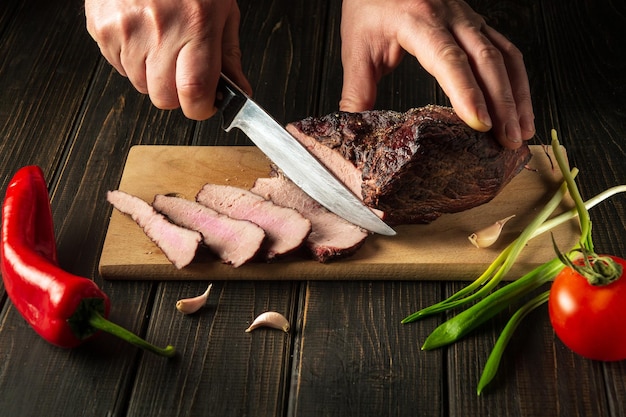 Chef cuts the baked beef steak with a knife on a wooden table