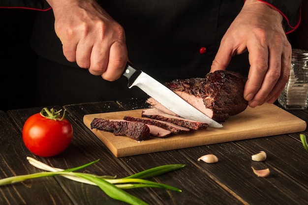 Photo chef cuts the baked beef steak with a knife on a wooden table