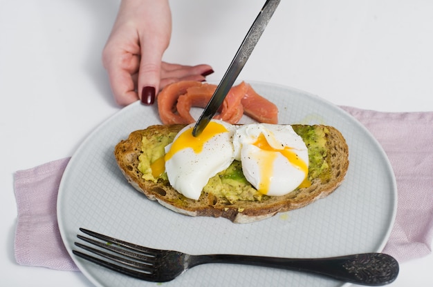 The chef cuts the egg on toast with avocado, salmon and black bread. 