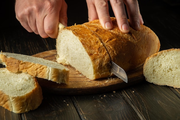 The chef cuts fresh bread with a knife on a kitchen cutting board